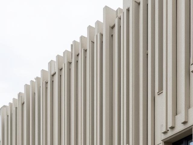 Moderne Architekturfassade verkleidet mit langen, vertikalen, texturierten Keramikplatten in Grau- und Sandtönen.
